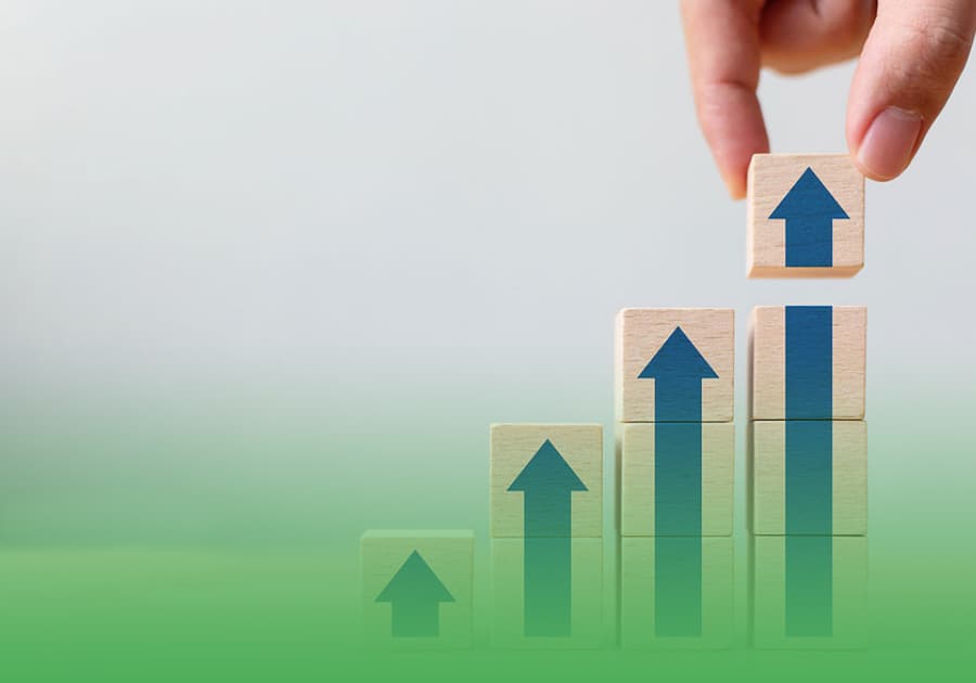 mcashadvance-investors-growth Wooden building blocks with a blue arrow, and a person's hand stacking the top block signify MCashAdvance providing you with the funding you need as a building block to grow your business